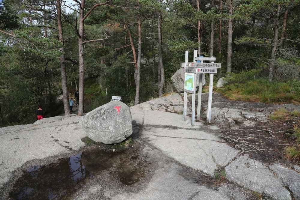 Trail junction at Preikestolen with wooden signposts and a red T marker on a boulder.