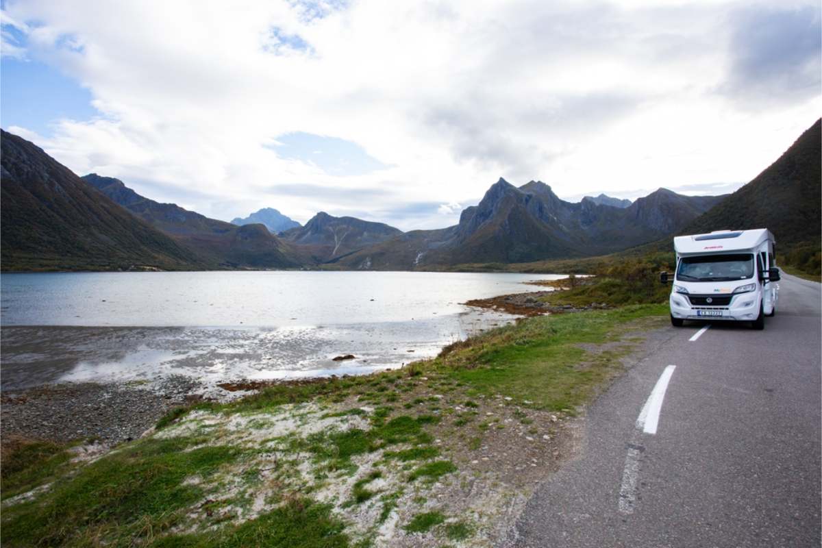 Beside a Norwegian fjord White motorhome on the roadside next to still fjord water, with jagged mountains along the far shore