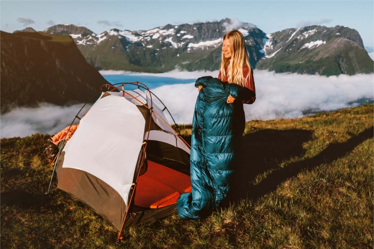 Woman unrolling a teal sleeping bag Woman unrolling a teal sleeping bag beside a small tent on a grassy ridge