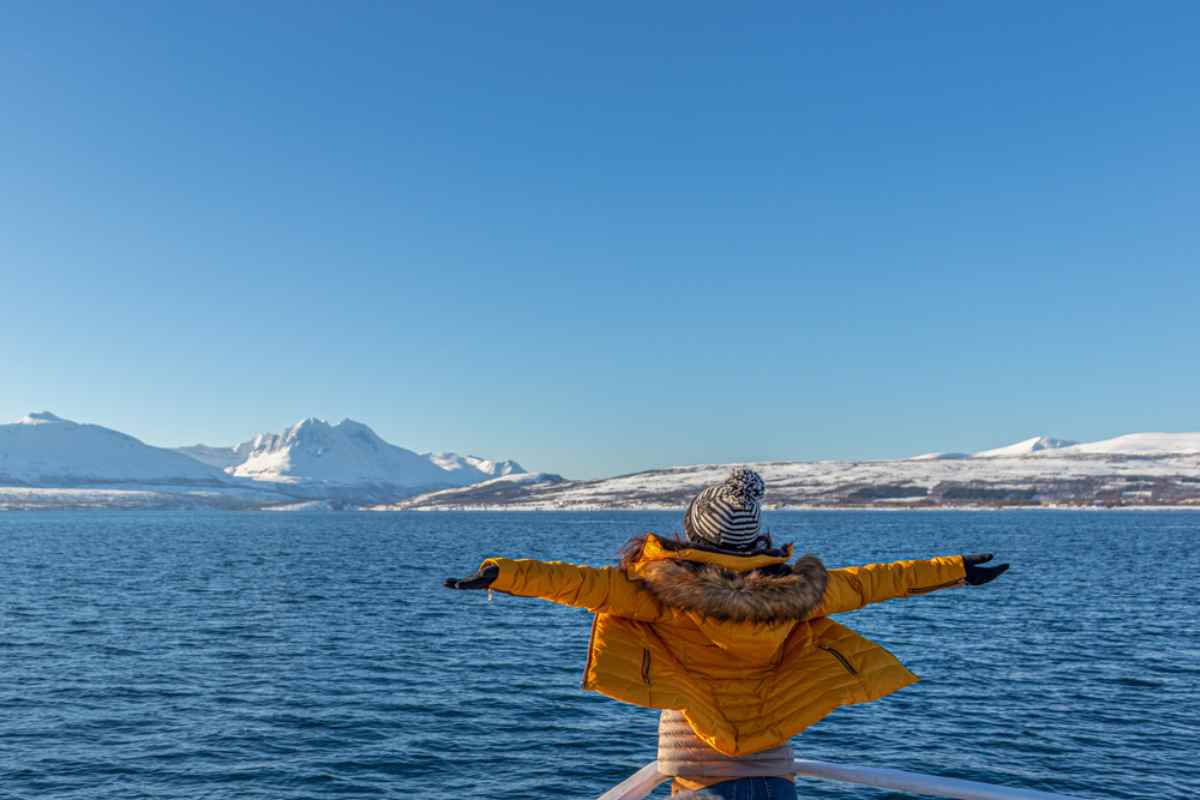 Traveler in a yellow jacket enjoying the Arctic sea and snowy fjords in Tromsø.