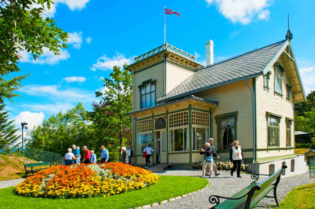 Troldhaugen, the former home of composer Edvard Grieg in Bergen, with a flower garden and visitors outside.