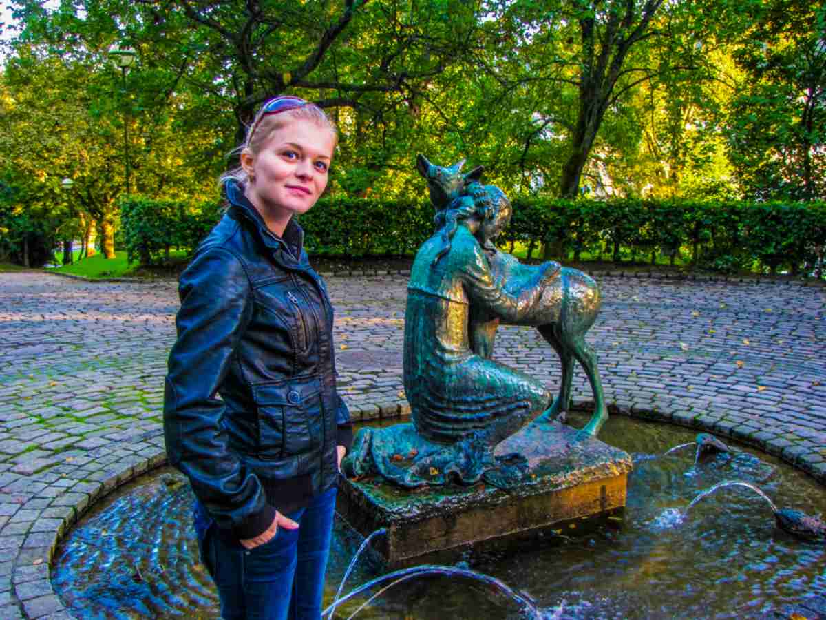 Statue of a girl with a deer in a fountain at Nygardsparken, Bergen, with a visitor standing nearby.