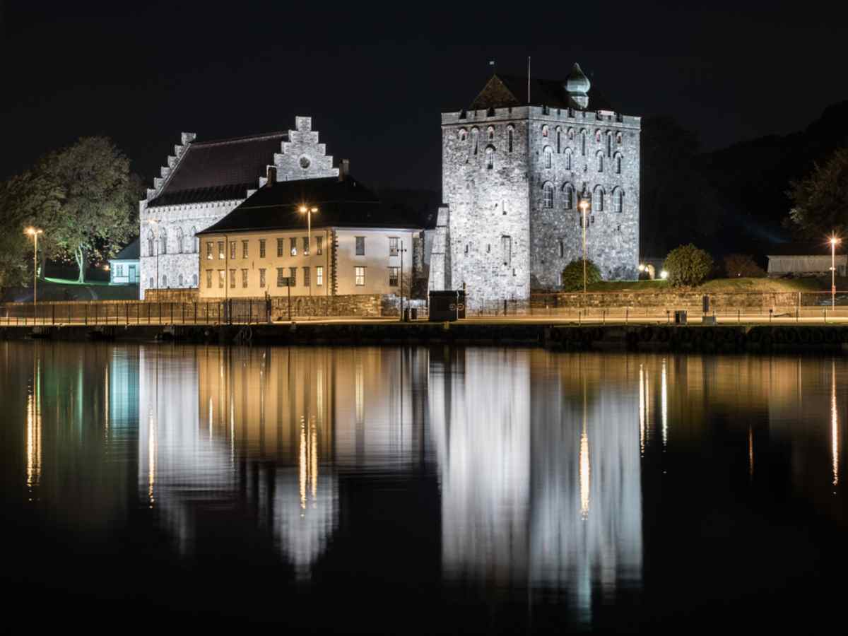 Night view of Bergenhus Fortress with reflections on the water.