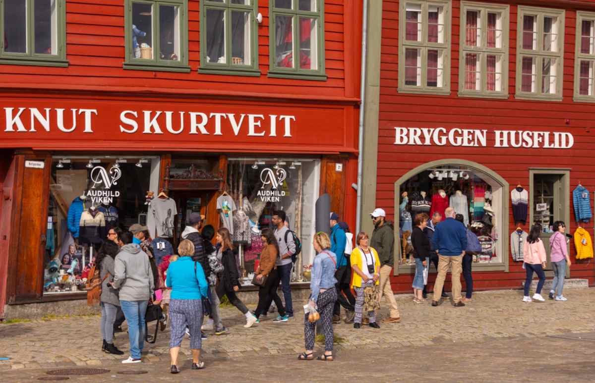 Colorful shops at Bryggen Wharf in Bergen with tourists walking by.