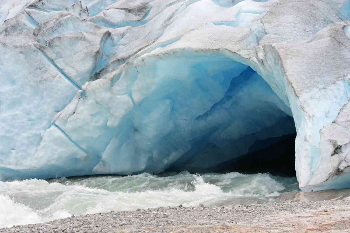 Blue ice cave in Norway Blue ice cave at Jostedalsbreen glacier with meltwater rushing out across a rocky shoreline