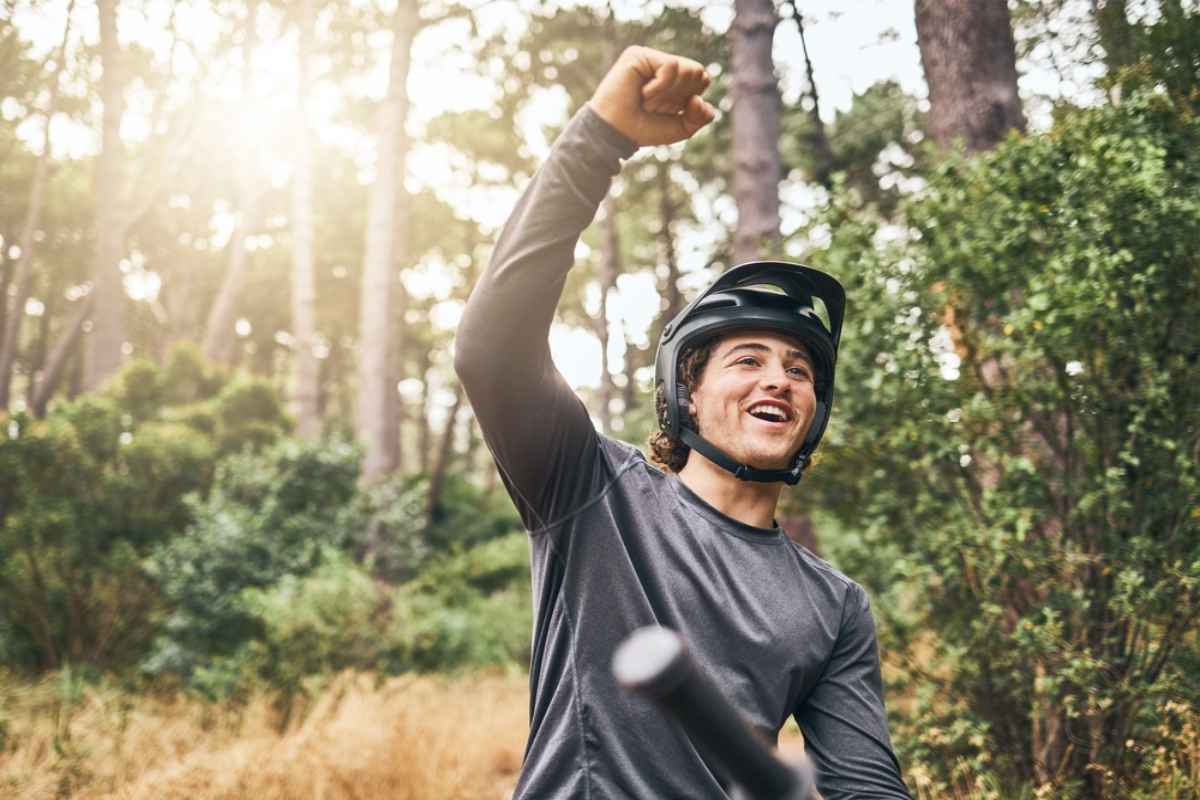 Biking in Norway's Roros Smiling mountain biker in a helmet raising a fist on a forest trail, celebrating a ride outdoors.