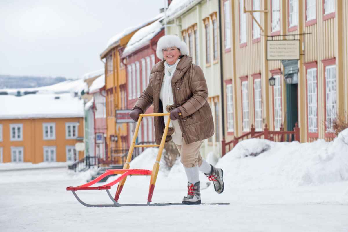 Kick sked in Roros Person using a kick sled on a snowy street in Røros, with colorful wooden houses lining the road in winter.
