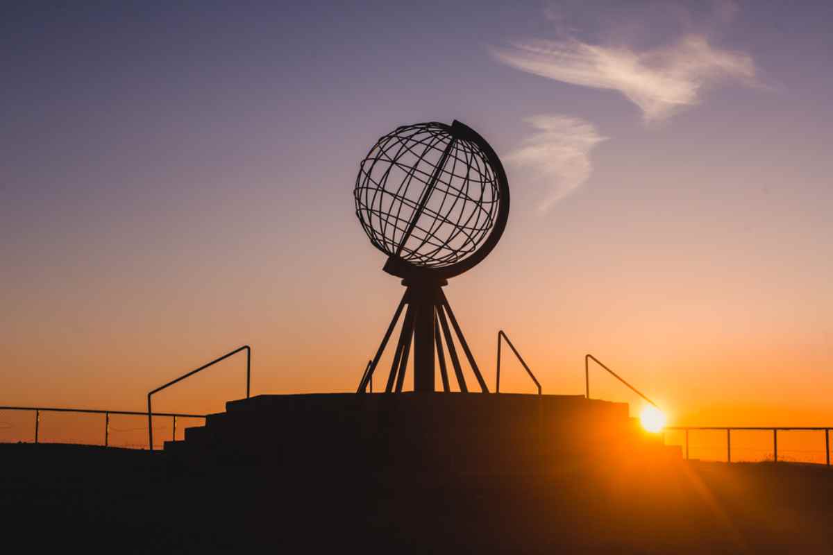 Silhouette of the North Cape Globe Monument at sunset, against an orange and purple sky.