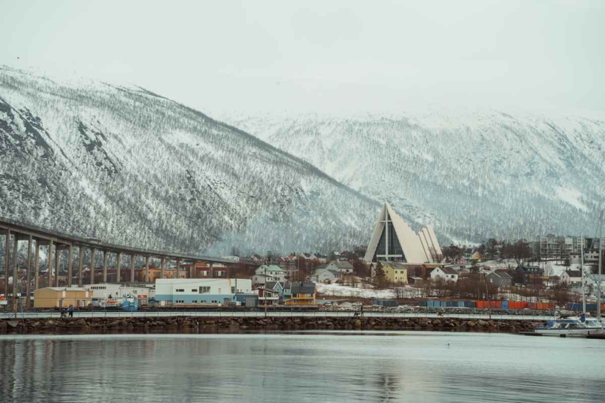 View of Tromsø’s waterfront with the Arctic Cathedral and bridge, snow-capped mountains behind.
