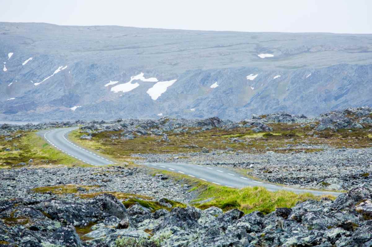 Rocky coastal landscape with sparse vegetation and a narrow road winding along the shoreline.