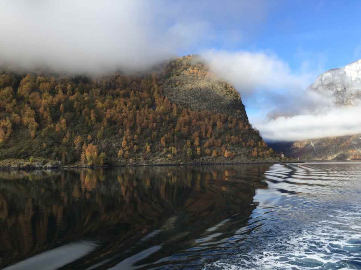 A view at water level of the Aurlandfjord in Norway, with somewhat turbulent waters and clouds covering the surrounding mountains.