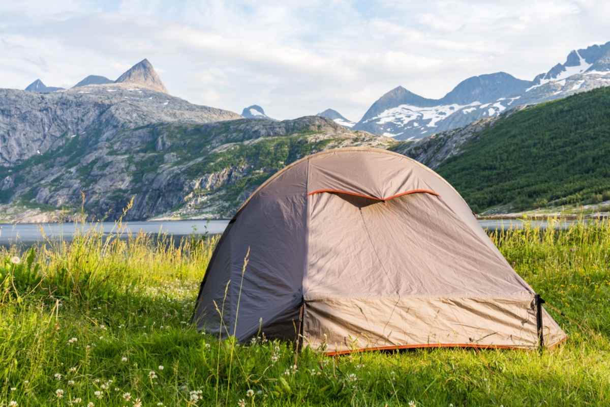 Dome tent on a grassy meadow by a fjord, with snow-streaked mountains near Ålesund, Norway.