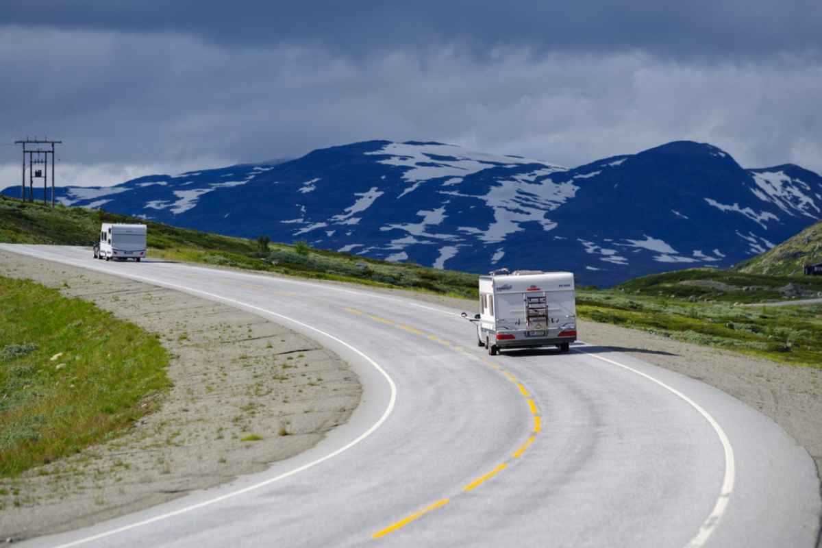 Stunning drone view of Norway's RV7 road as it passes through Hardangervidda above several sunlit clouds on a beautiful clear day.