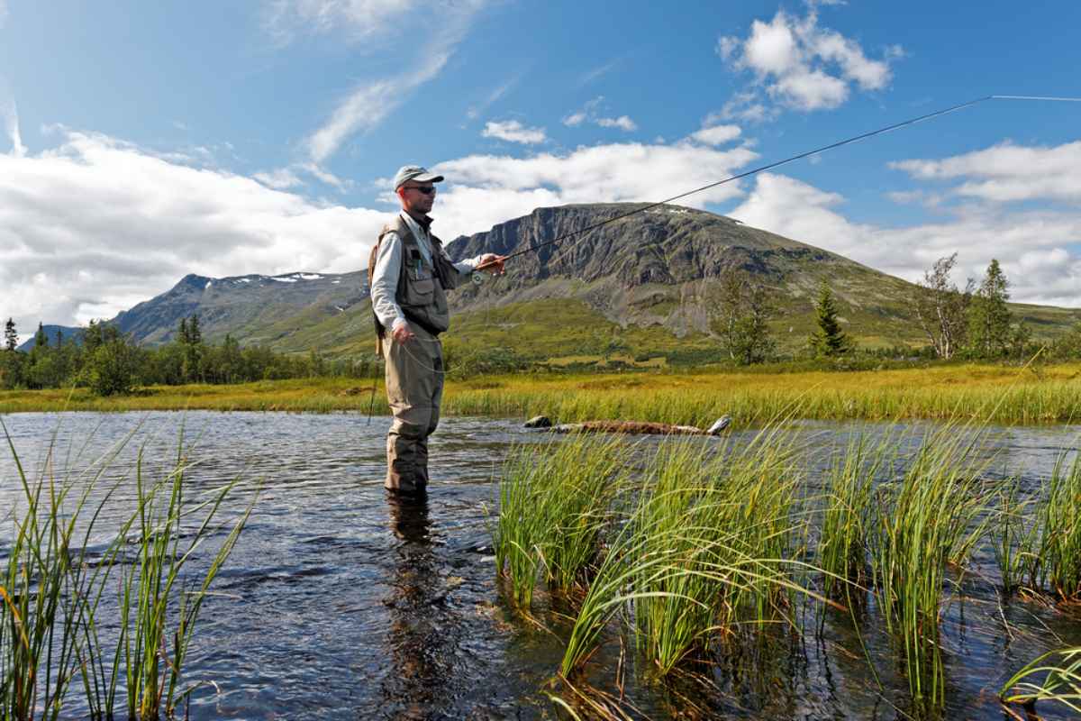 Man fly fishing in a clear river along Norway’s RV52 road with mountains in the background.