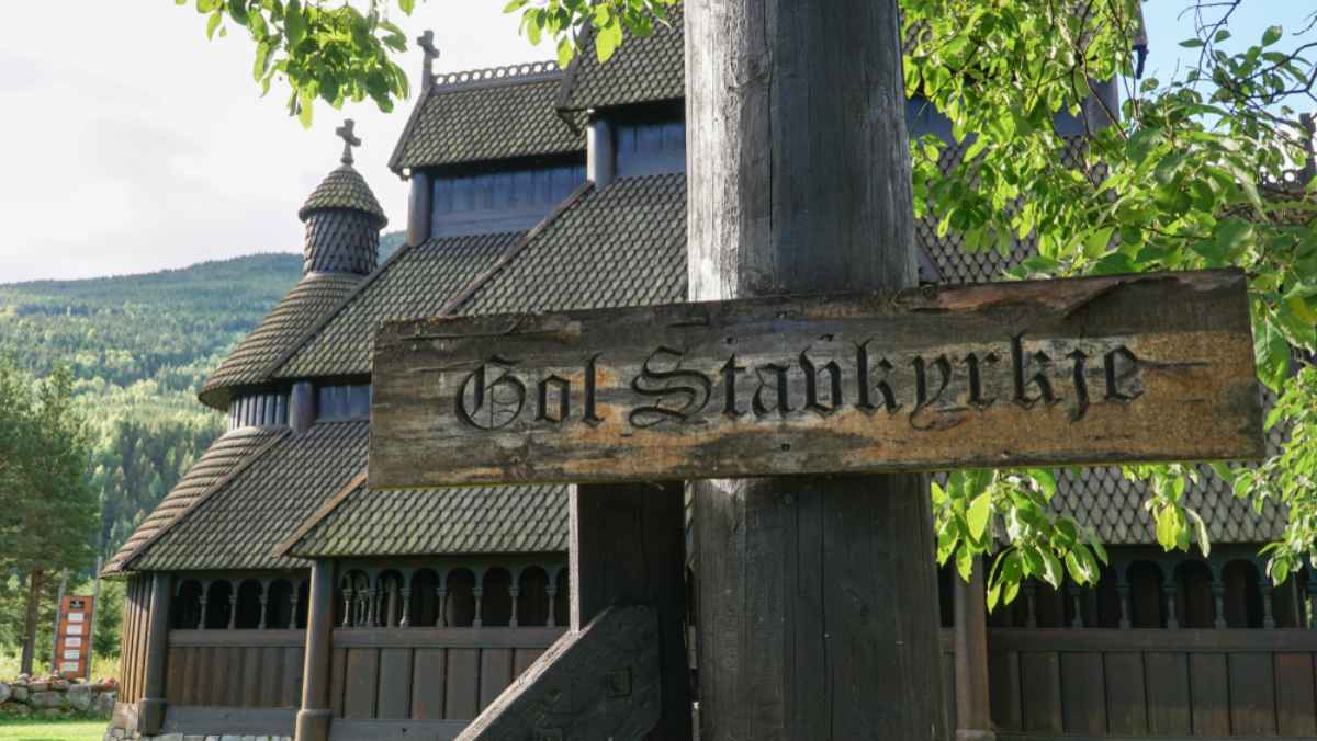 Wooden sign for Gol Stave Church with the historic stave church in the background in Norway.