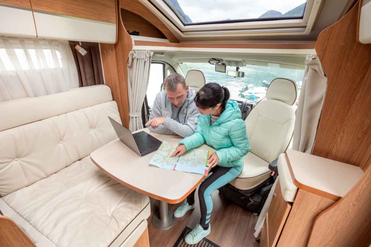 Couple inside a motorhome using a laptop and map to plan their route through Norway.