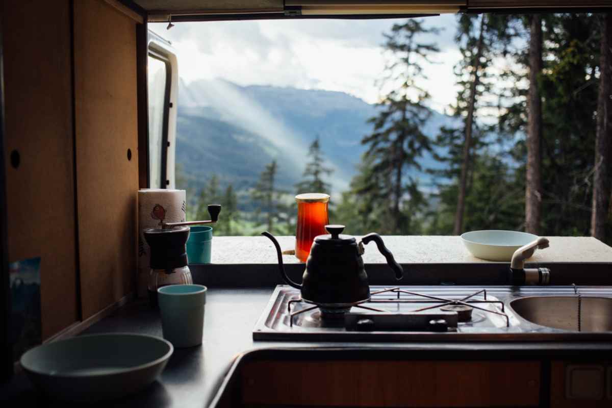 Simple campervan kitchen with kettle and cups looking out to forested mountains and valley.