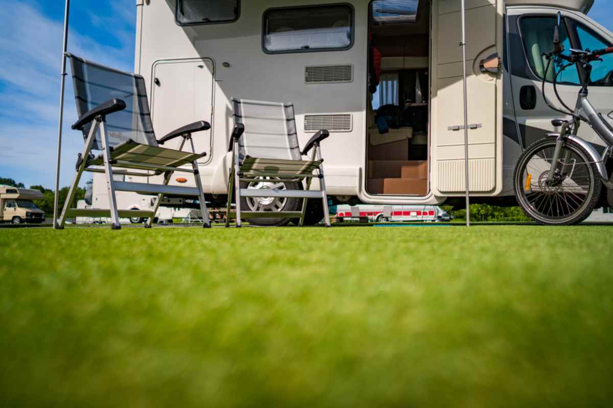 Two folding chairs and a bicycle outside a parked motorhome on green grass under blue sky.