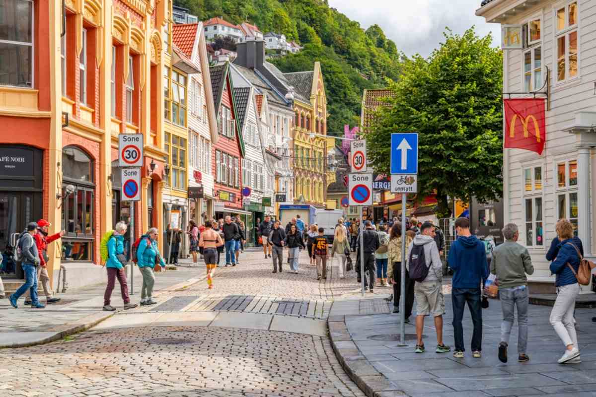 Bergen, Norway Colorful wooden houses and a cobbled street in Bergen’s historic center, pedestrians strolling beneath speed signs near Bryggen on a bright day.