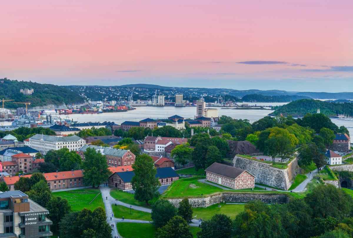 Oslo in Norway Panoramic view of Oslo and the harbor at sunset, Akershus Fortress and green parks in the foreground, islands and city skyline around the bay.