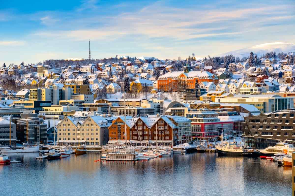 Tromsø, Norway Winter view of Tromsø harbor with snow-covered rooftops, wooden warehouses, and moored boats, soft morning light on the Arctic city and hills.
