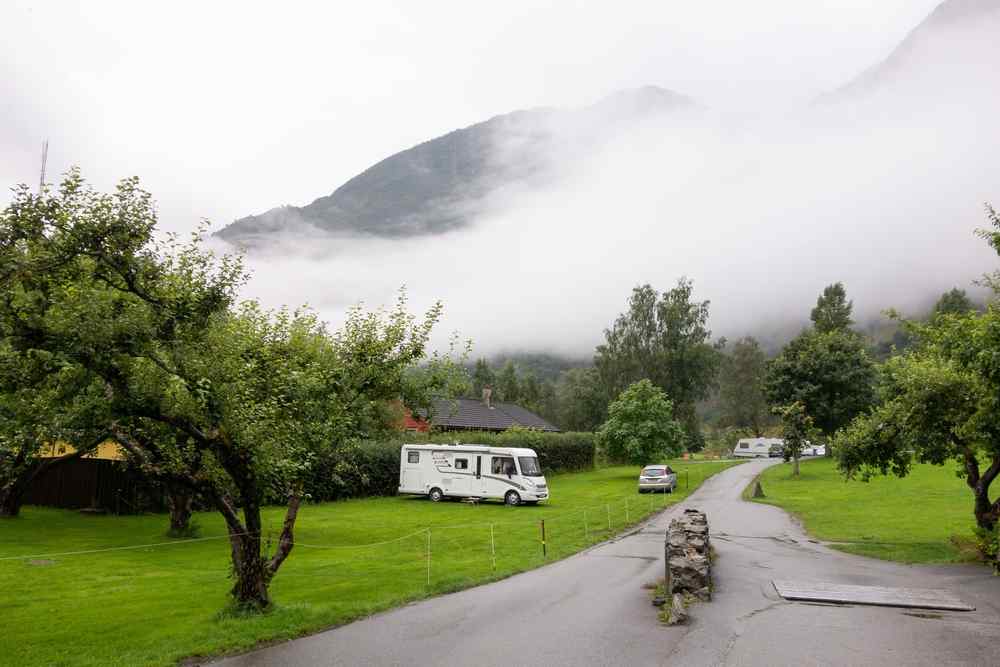 Renting a campervan in Flam, Norway Motorhome on a grassy campground in Flåm with low clouds covering the surrounding mountains.