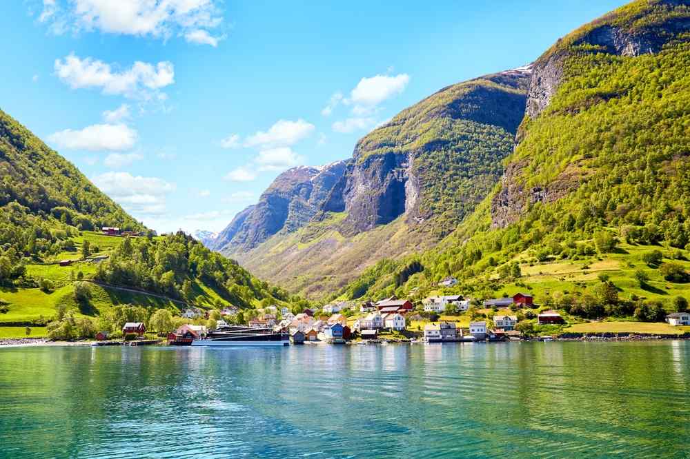 Flam in Norway View of Flåm village beside the fjord, framed by lush mountains under a blue sky.