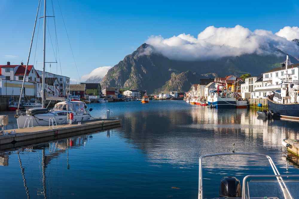 Lofoten islands' skyline Fishing boats and colorful waterfront buildings in a peaceful Lofoten harbor surrounded by steep mountains and low clouds.